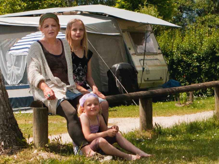 Mutter sitzt mit ihren beiden Kindern auf einem Campingplatz