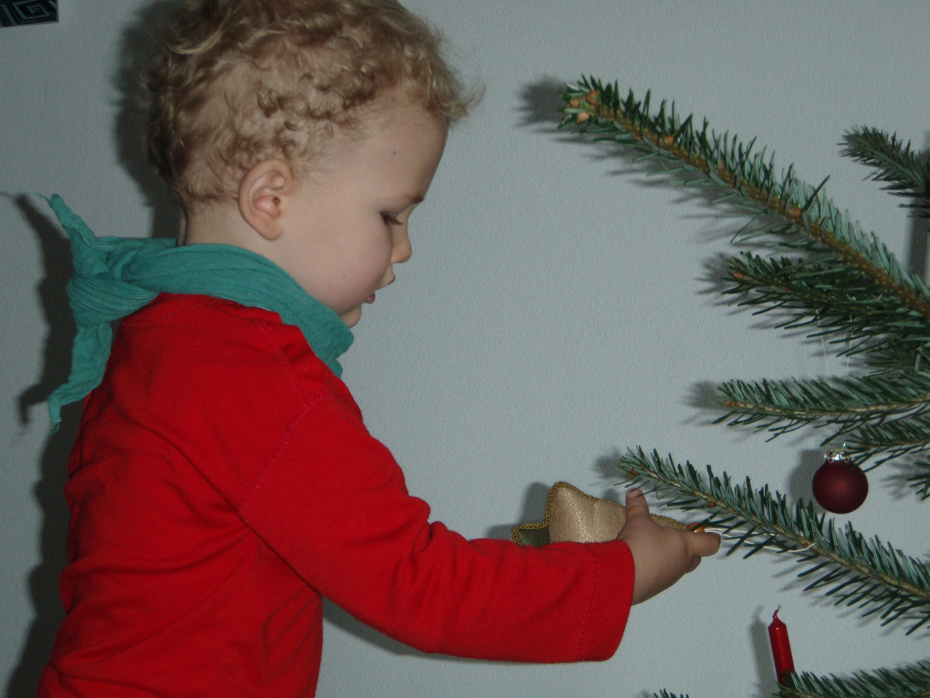 Ein kleiner Junge hängt Weihnachtsschmuck an den Baum