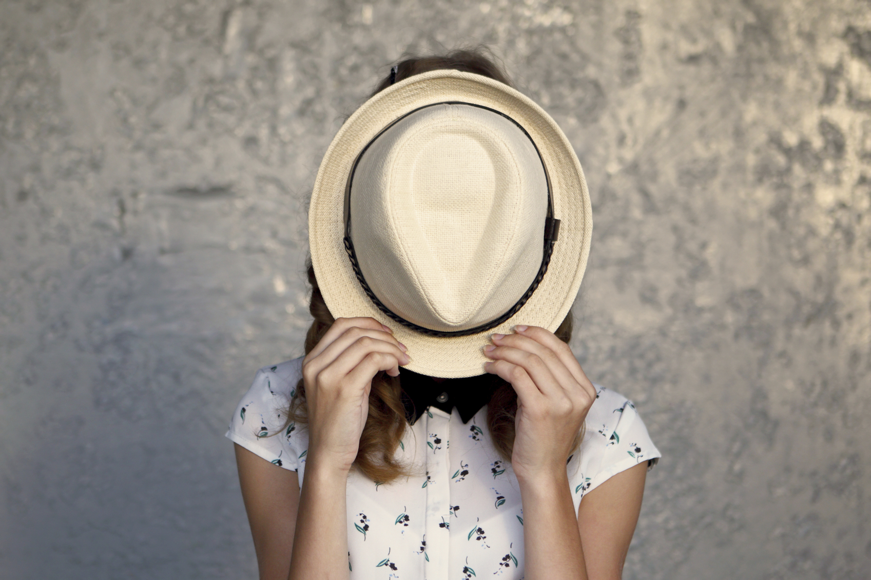 Frau versteckt ihr Gesicht hinter einem Hut