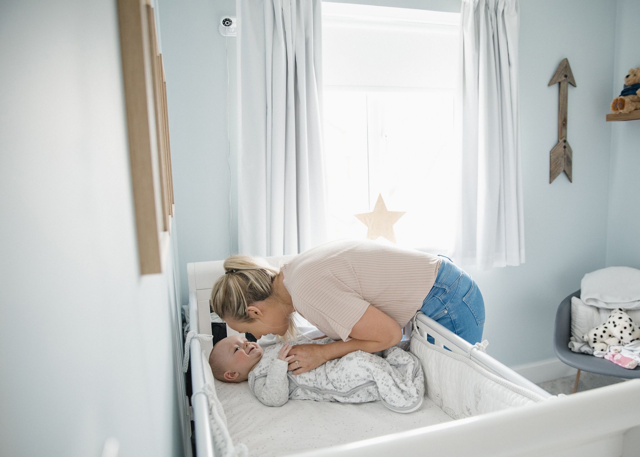 Dank höhenverstellbarem Lattenrost am Gitterbett beugt sich die Mutter nur wenig über den Rand zu ihrem Baby.