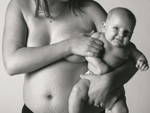 Frau mit Schwangerschaftsstreifen am Bauch hält ihr Kind im Arm