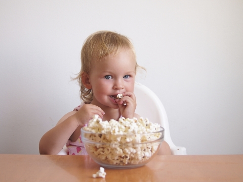 Kleinkind isst Popcorn aus einer Glasschüssel