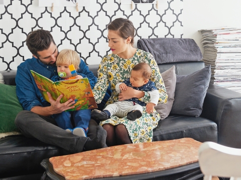 Familie Baumann sitzt im Wohnzimmer und schaut ein Buch an