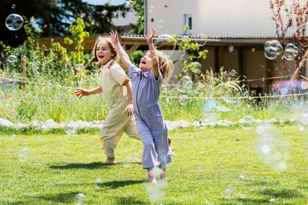 Zwei Kinder spielen in einem Garten mit Seifenblasen.