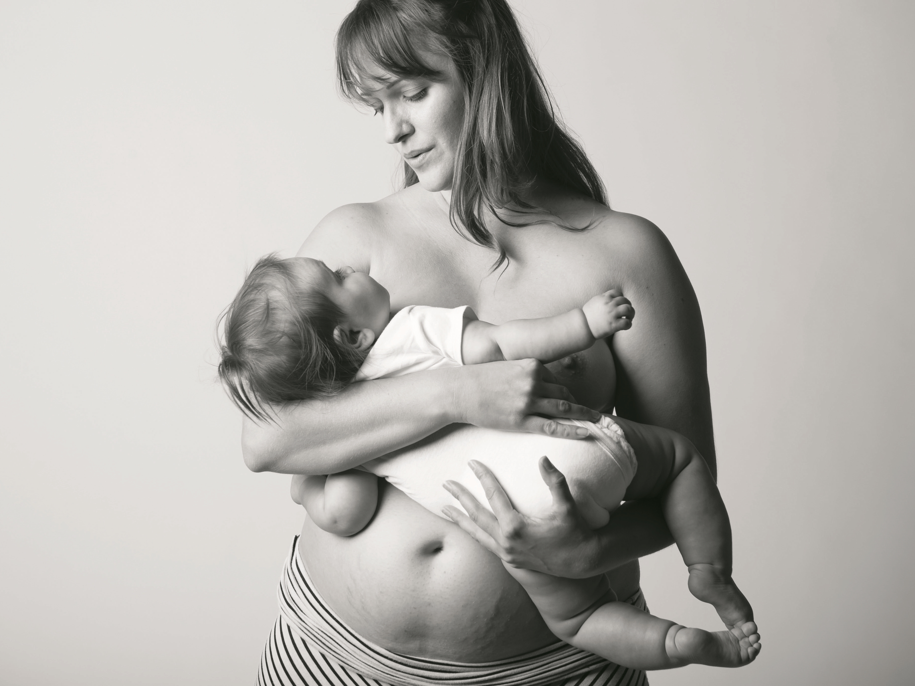 Frau mit Dehnungsstreifen am Bauch hält ihr Kind im Arm