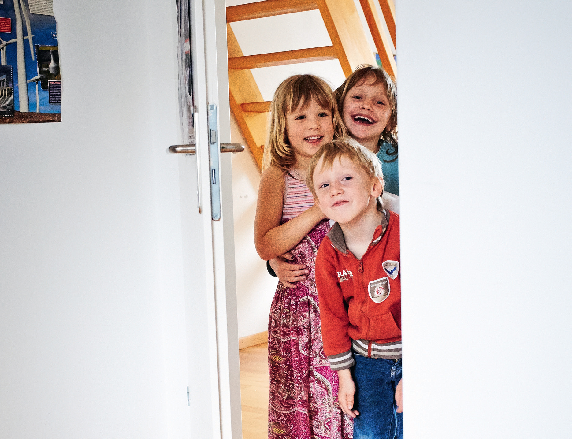 Ein Junge und zwei Mädchen schauen durch die Zimmertür in einen Raum hinein