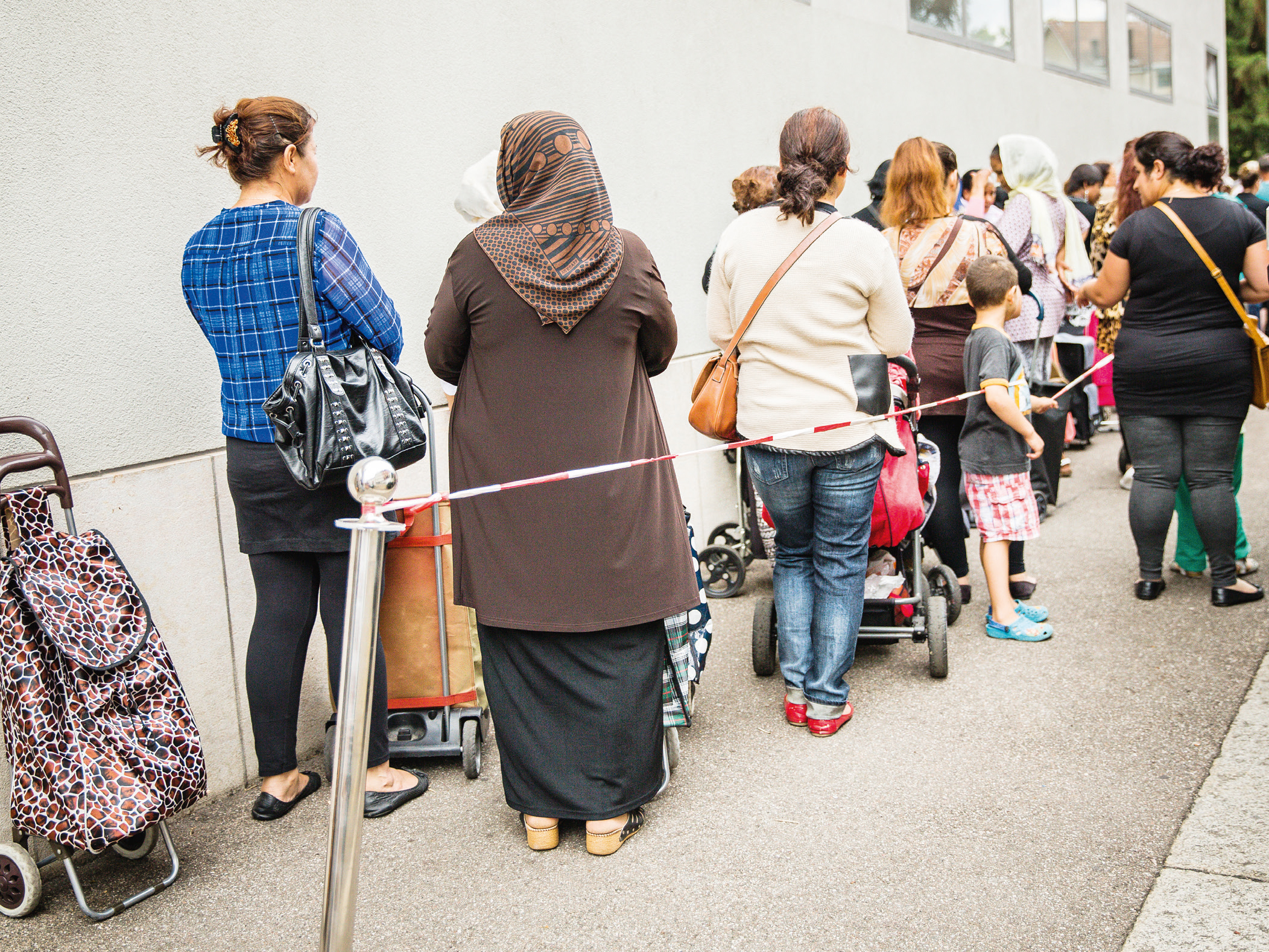 Menschen stehen an, man sieht sie von hinten