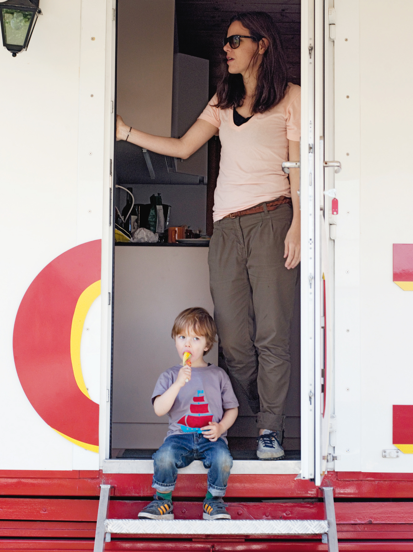 Kind sitzt vor dem Wohnwagen und isst ein eis