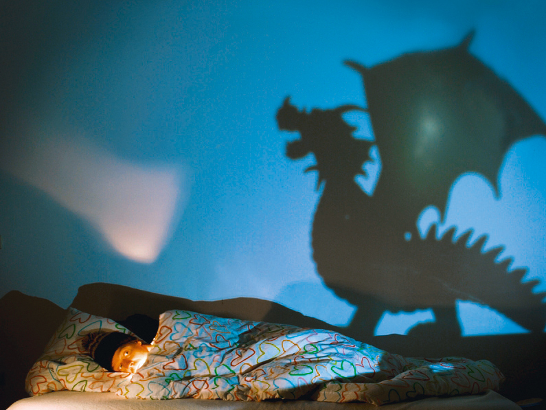 Kind im Bett, auf der Mauer einen Schatten in Form eines Drachens