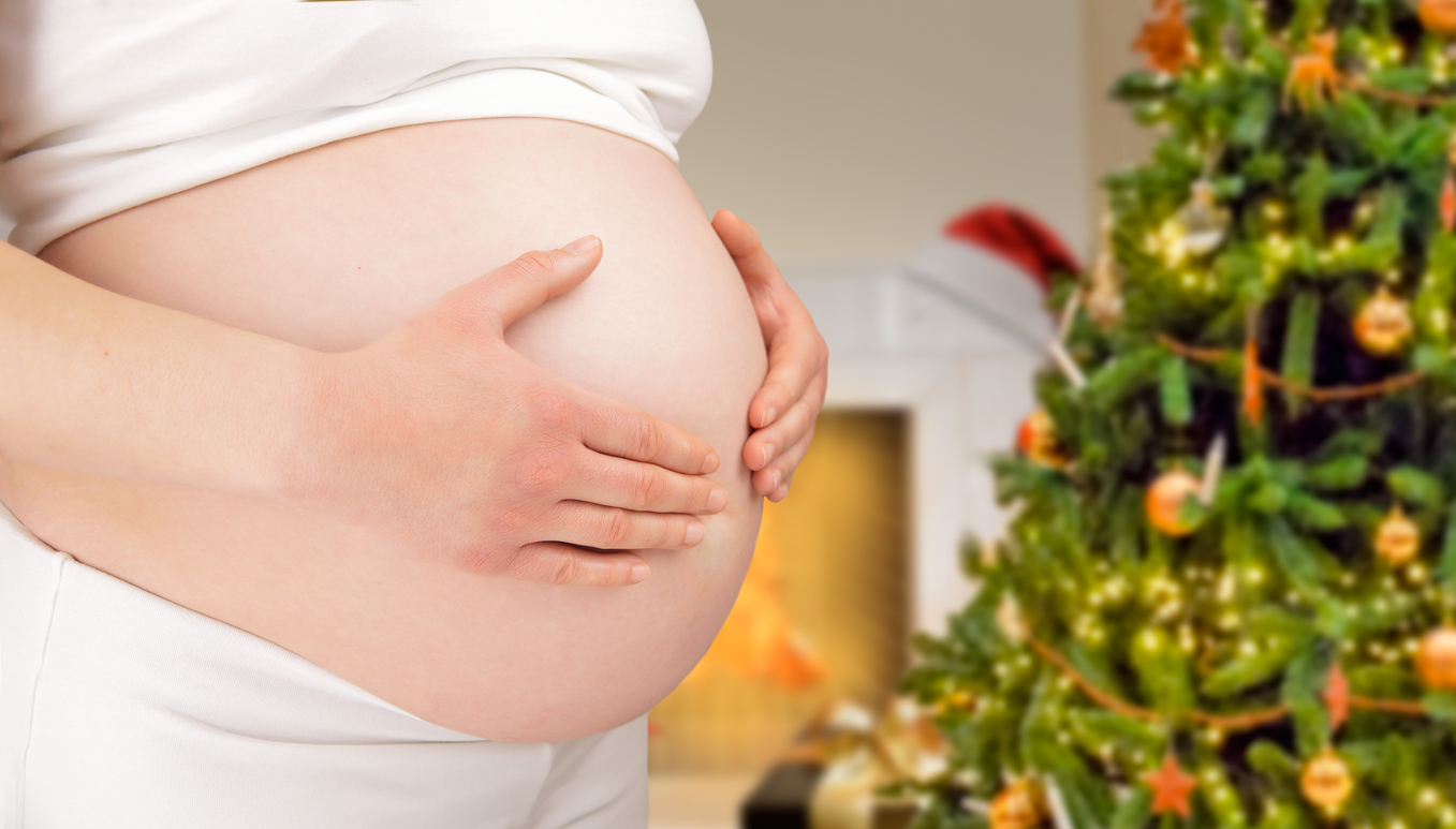 Schwangerer Bauch vor Weihnachtsbaum