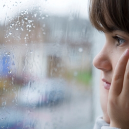 Kind schaut durch von Regen benetzte Fensterscheibe nach draussen