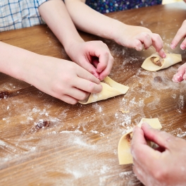 Zwei Kinder und eine erwachsene Person machen frische Pasta