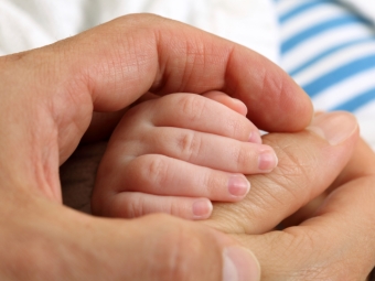 Babyhand wird von Händen von Mutter und Vater umschlossen