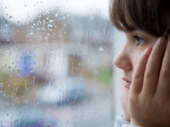 Kind schaut durch von Regen benetzte Fensterscheibe nach draussen