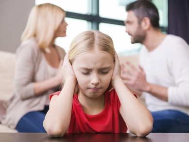 Ein Mädchen hält sich die Ohren zu, während im Hintergrund die Eltern streiten