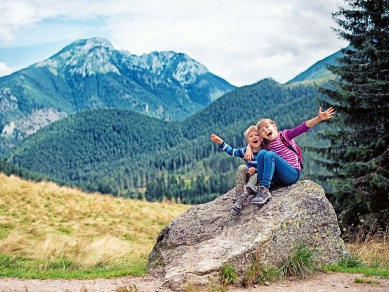 zwei kinder mit wanderschuhen auf einem felsblock in den bergen