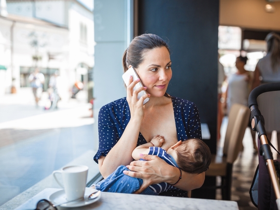 Eine Mutter stillt ihr Baby im Café während sie am Handy spricht.