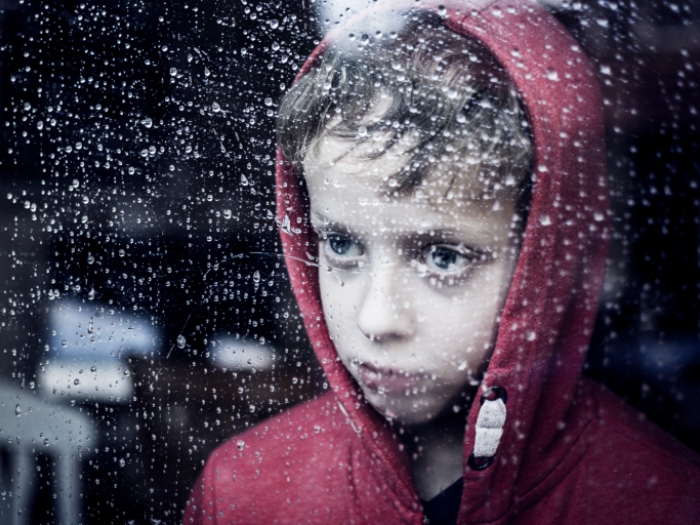 Junge schaut durch regennasse Scheibe nach draussen
