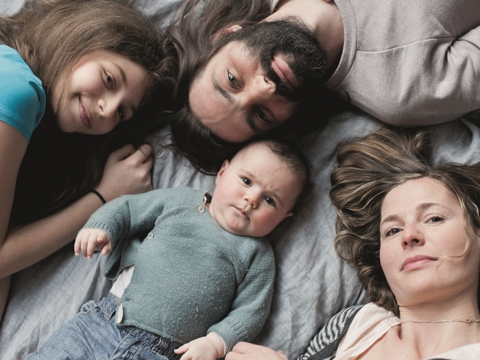 Familie liegt auf dem Bett, von oben fotografiert.