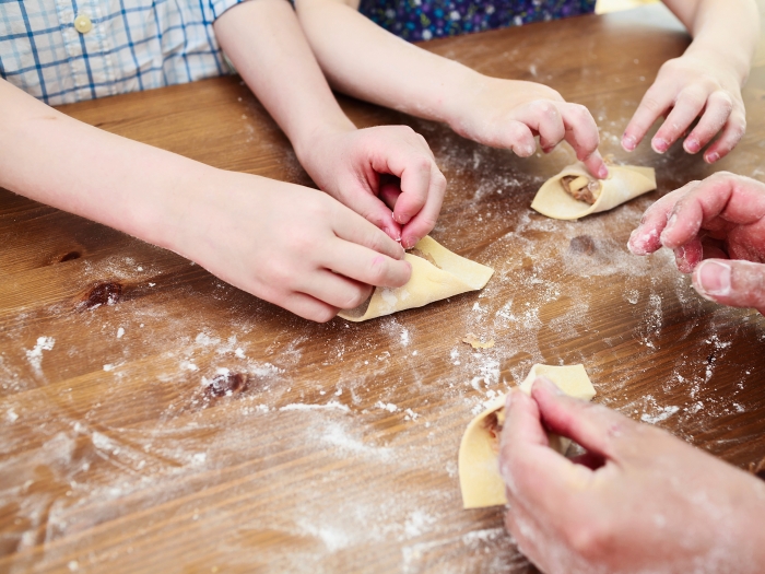 Zwei Kinder und eine erwachsene Person machen frische Pasta