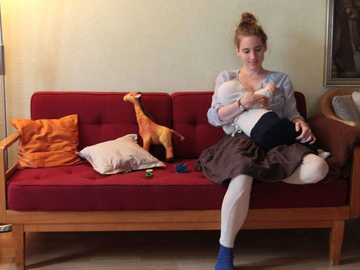 Frau sitzt auf einem Sofa und stillt ihr Kind