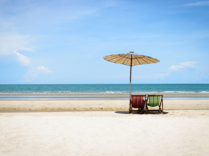 Zwei Liegestühle und ein Sonnenschirm an einem einsamen Strand am Meer