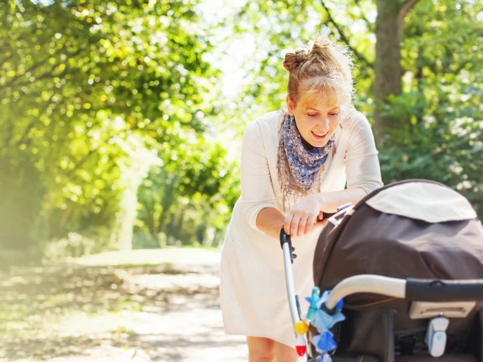 Mutter bückt sich zum Kind im Kinderwagen 