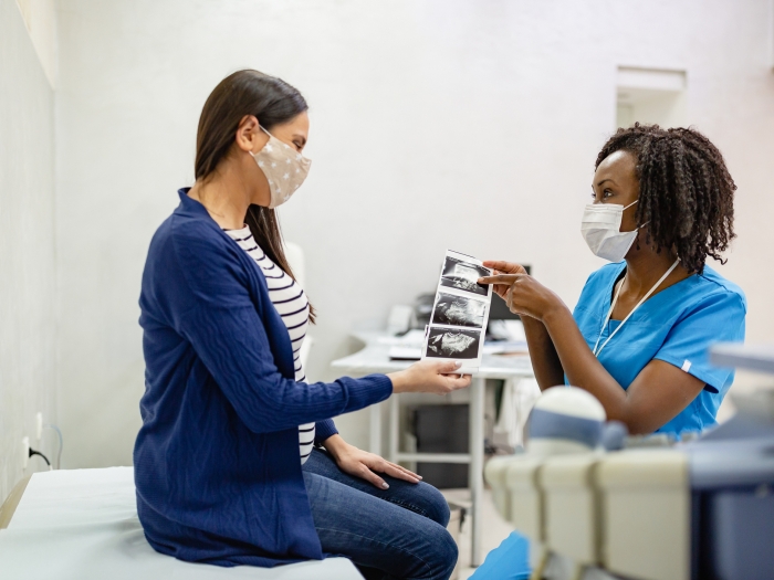 Schwangere in Maske mit Ultraschallbildern