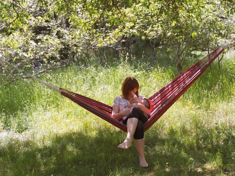 Stillende Mutter sitzt in der Hängematte im Garten