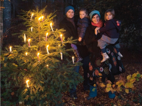 Familie im Wald hinter einer mit brennenden Kerzen ausgestatteten Tanne