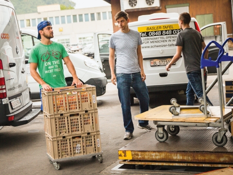 Zwei Zivildienstleistende transportieren Waren auf Rollwagen