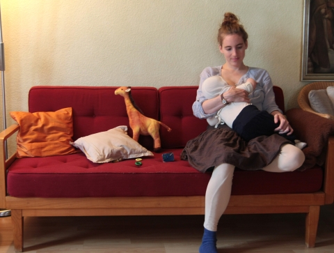 Frau sitzt auf einem Sofa und stillt ihr Kind
