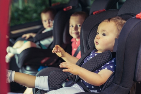 Drei Kinder auf dem Rücksitz in Kinderautositzen.