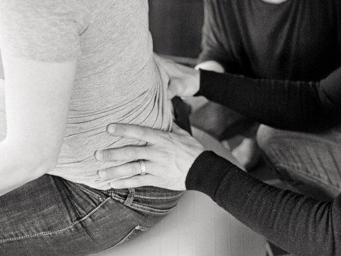 Die Doula zeigt dem werdenden Vater, wie er Rückenschmerzen seiner schwangeren Partnerin lindern kann