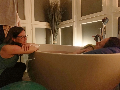 Die Doula Martina Dolder betrachtet Mutter und Neugeborenes in der Badewanne